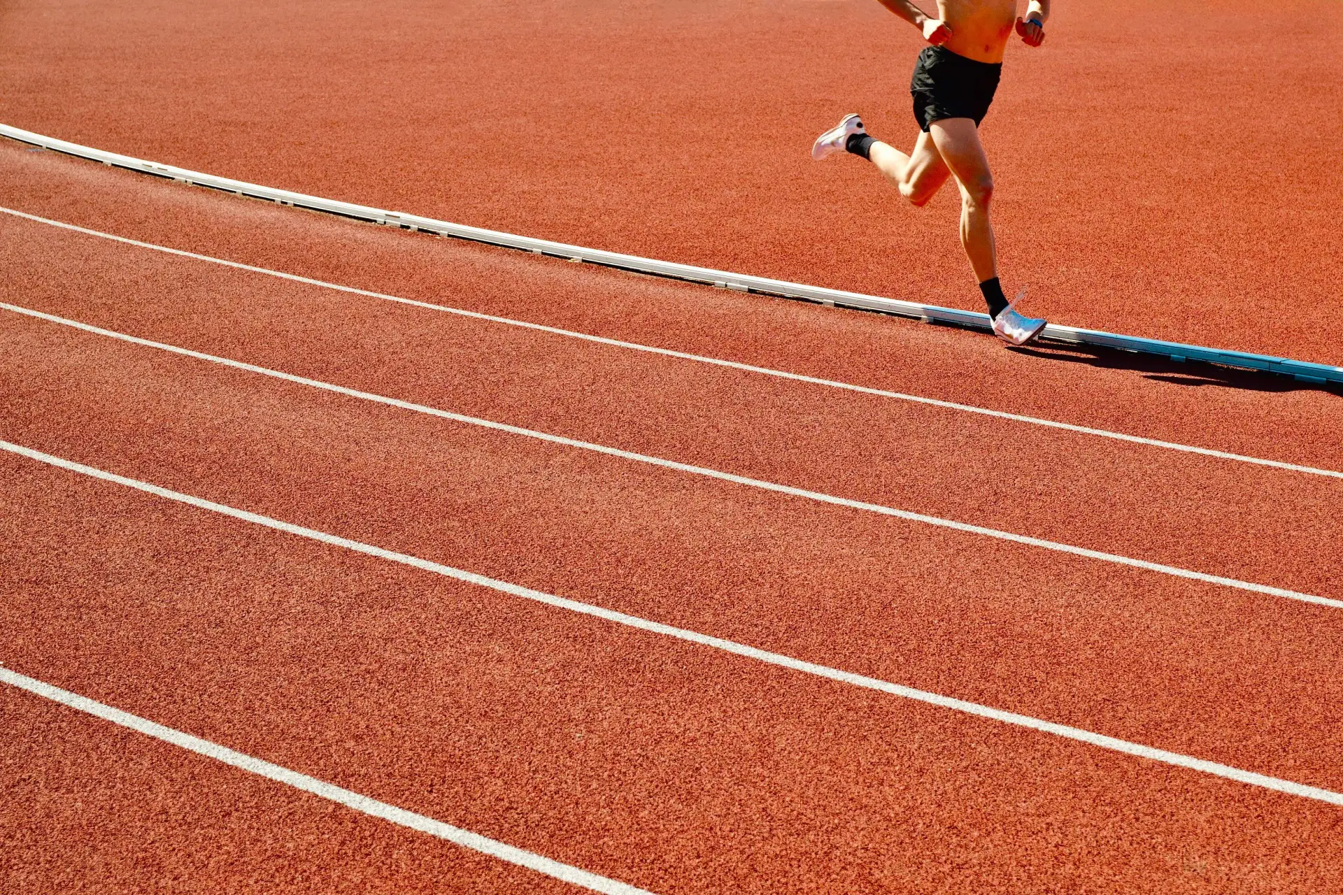 A runner mid-stride on a red running track
